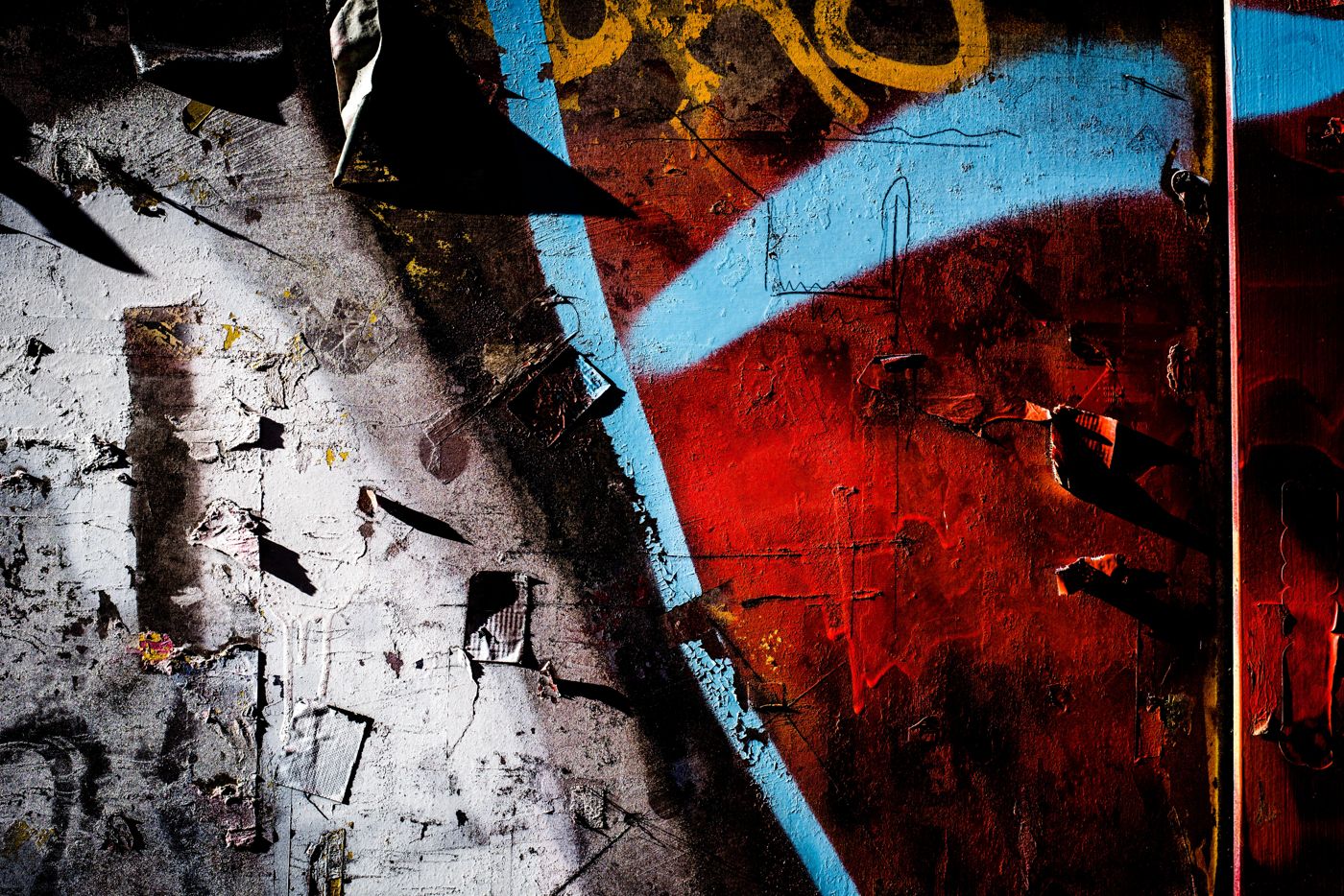 Torn posters and spray paint on a city wall, white, red and blue